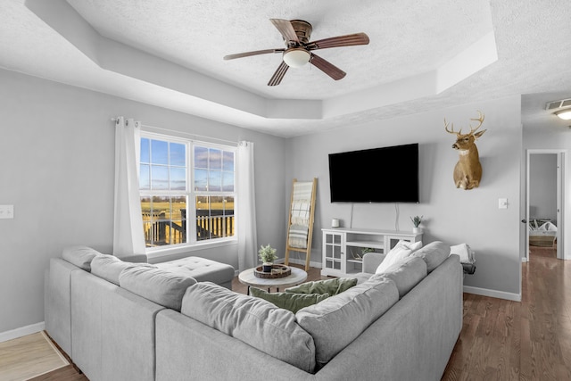 living room featuring a tray ceiling, ceiling fan, a textured ceiling, and hardwood / wood-style flooring