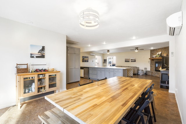 dining room with ceiling fan, a stone fireplace, and a wall unit AC