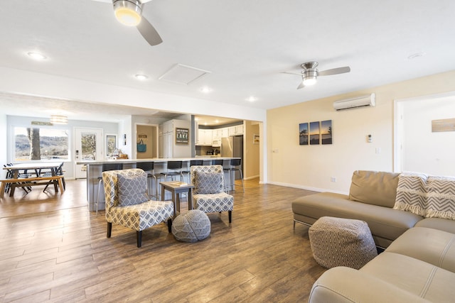 living area with ceiling fan, a wall unit AC, wood finished floors, and attic access