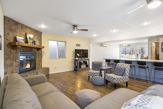 living area with attic access, ceiling fan, a stone fireplace, and wood finished floors