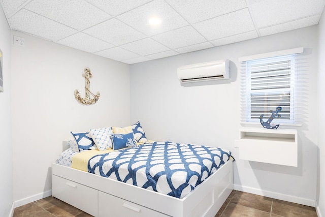 bedroom with dark tile patterned flooring, a wall mounted AC, a paneled ceiling, and baseboards