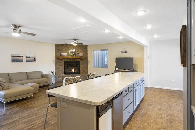 kitchen with ceiling fan, a stone fireplace, wood-type flooring, a breakfast bar area, and a kitchen island