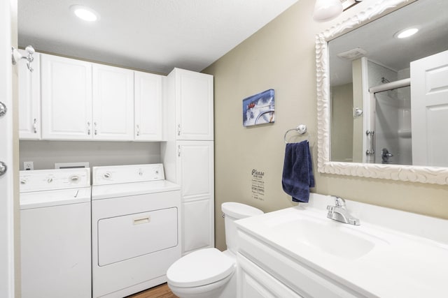 bathroom featuring washing machine and dryer, a textured ceiling, toilet, a shower with door, and vanity