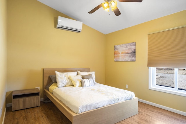 bedroom featuring ceiling fan, a wall unit AC, wood finished floors, and baseboards