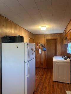 kitchen with washer / dryer, hardwood / wood-style flooring, wood walls, and white refrigerator