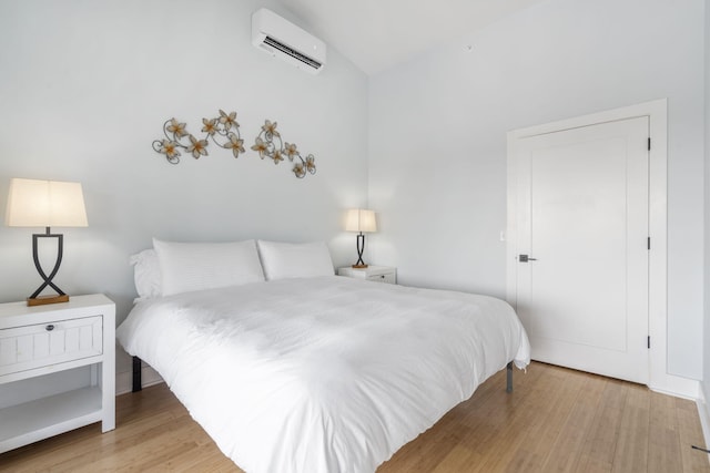 bedroom with a wall unit AC, vaulted ceiling, and light wood-style flooring
