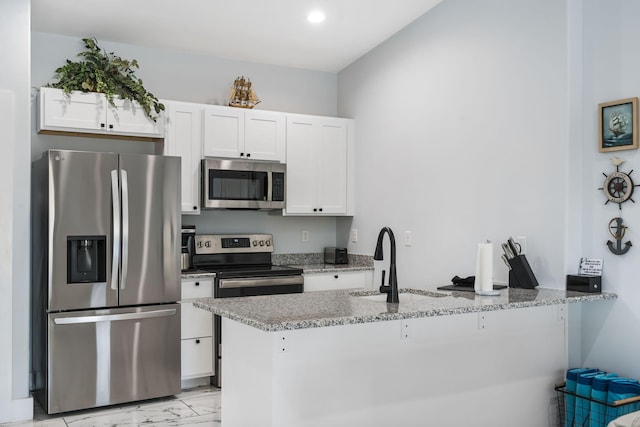kitchen featuring stainless steel appliances, a peninsula, a sink, white cabinetry, and light stone countertops