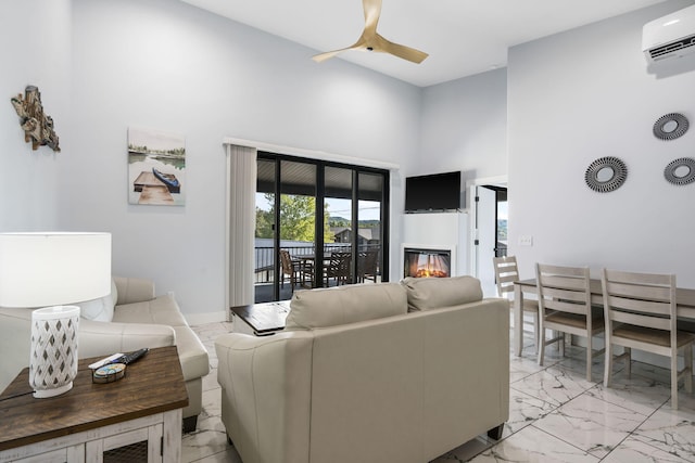 living room with ceiling fan, a high ceiling, marble finish floor, a wall mounted air conditioner, and a glass covered fireplace