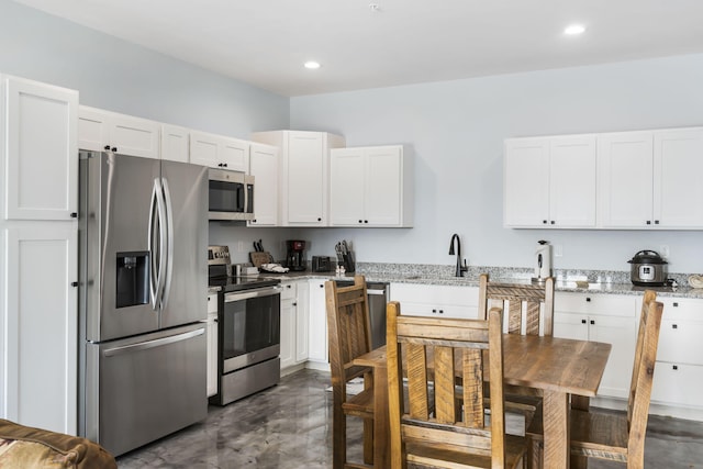 kitchen with appliances with stainless steel finishes, finished concrete floors, white cabinetry, and light stone countertops