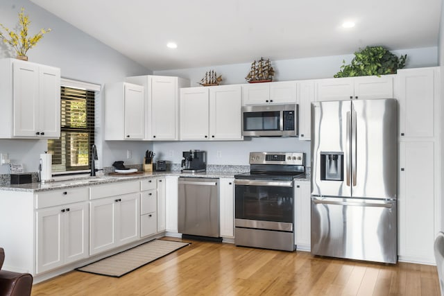 kitchen with appliances with stainless steel finishes, light wood-type flooring, white cabinetry, and light stone counters
