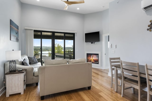 living room featuring light wood-type flooring, a high ceiling, a glass covered fireplace, and a wall mounted AC