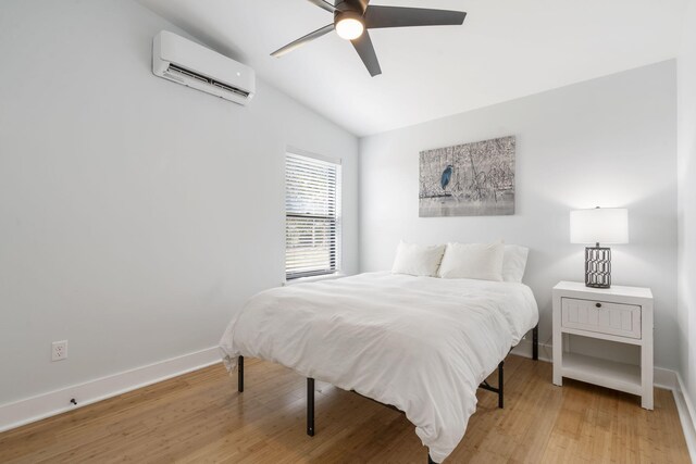 bedroom featuring ceiling fan, baseboards, vaulted ceiling, an AC wall unit, and light wood finished floors