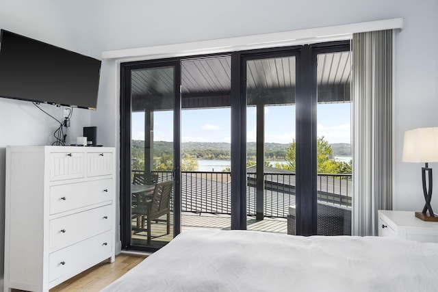bedroom featuring access to exterior, a water view, and light wood-style flooring