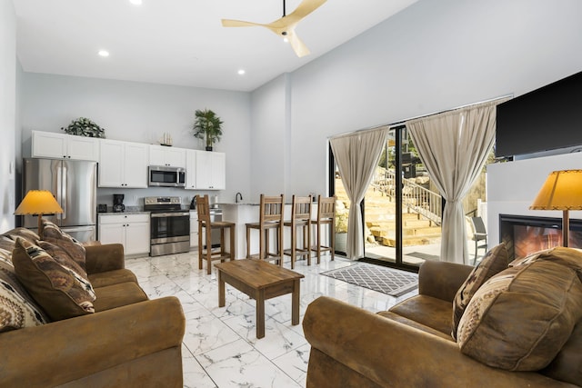 living room featuring marble finish floor, a high ceiling, a ceiling fan, and recessed lighting
