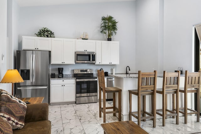 kitchen featuring marble finish floor, appliances with stainless steel finishes, white cabinets, and light stone counters