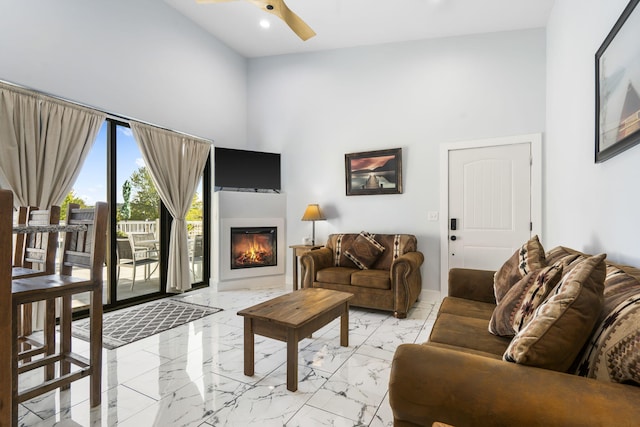 living room with a ceiling fan, marble finish floor, a lit fireplace, a high ceiling, and recessed lighting