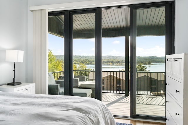 bedroom with a water view, access to outside, and wood finished floors
