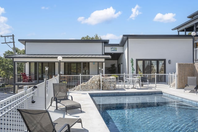 back of house featuring metal roof, fence, an outdoor pool, a standing seam roof, and a patio area