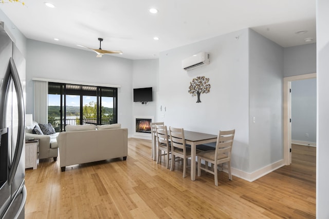 living room featuring recessed lighting, baseboards, a wall mounted AC, light wood-type flooring, and a glass covered fireplace