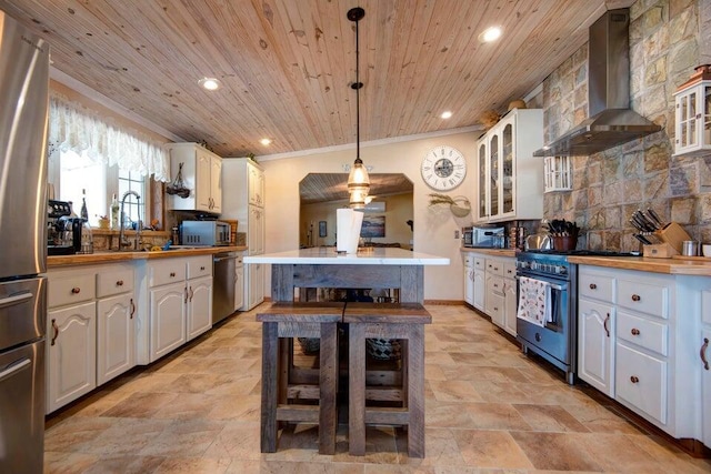 kitchen with hanging light fixtures, white cabinetry, stainless steel appliances, and wall chimney exhaust hood