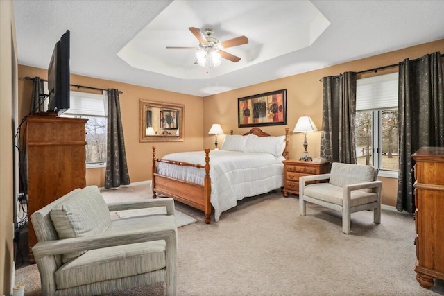 carpeted bedroom featuring a tray ceiling, multiple windows, and ceiling fan