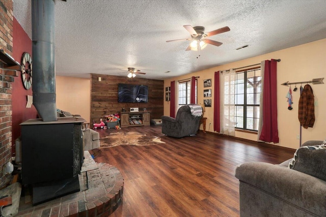 living room featuring a wood stove, ceiling fan, hardwood / wood-style floors, a textured ceiling, and wooden walls