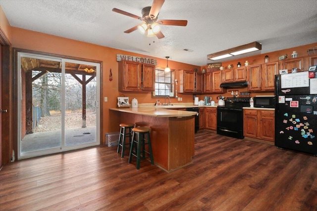 kitchen featuring kitchen peninsula, a breakfast bar, black appliances, dark hardwood / wood-style floors, and hanging light fixtures