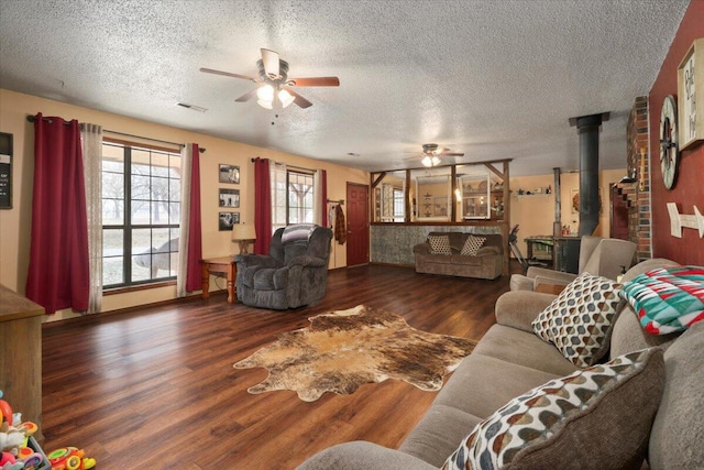 living room with a textured ceiling, dark hardwood / wood-style floors, a wood stove, and ceiling fan