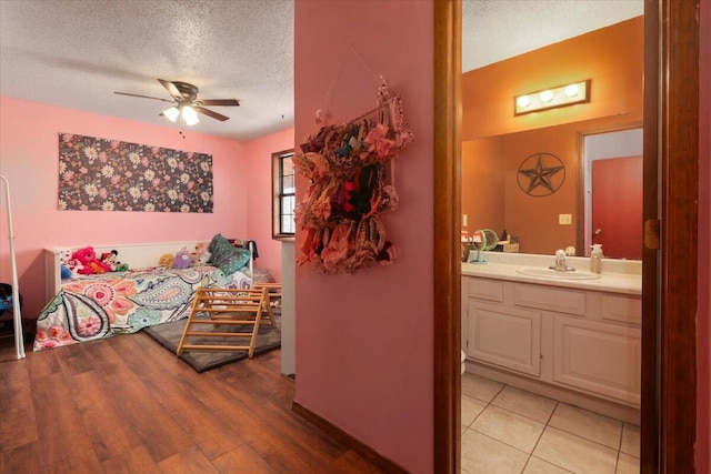 bedroom with ensuite bath, a textured ceiling, ceiling fan, sink, and light hardwood / wood-style flooring