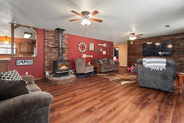 living room featuring a wood stove, ceiling fan, hardwood / wood-style floors, and a textured ceiling