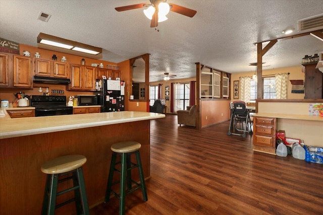 kitchen with dark hardwood / wood-style flooring, kitchen peninsula, a textured ceiling, a breakfast bar area, and black appliances