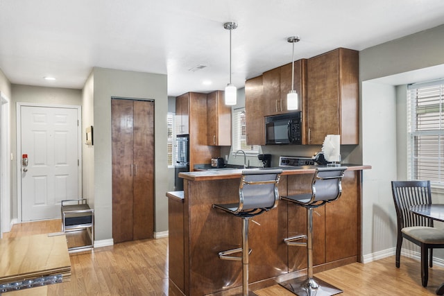 kitchen with sink, light wood-type flooring, decorative light fixtures, kitchen peninsula, and a breakfast bar area