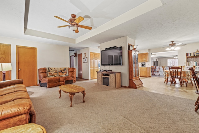 living room with a raised ceiling, ceiling fan, light carpet, and a textured ceiling