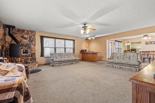 carpeted living room with ceiling fan, a wood stove, a textured ceiling, and track lighting