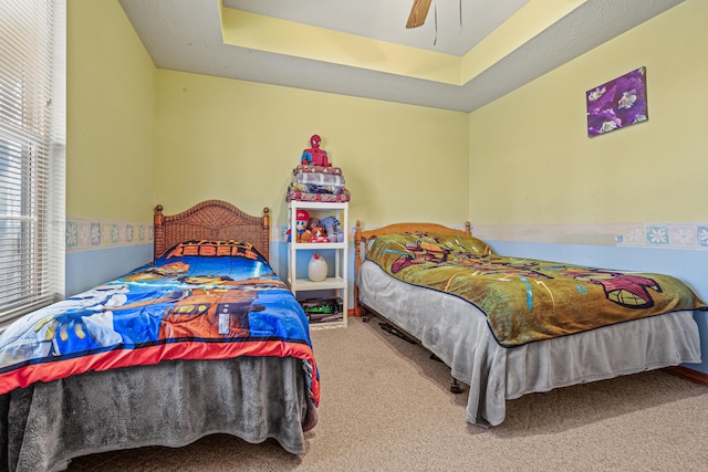 carpeted bedroom with a raised ceiling and ceiling fan