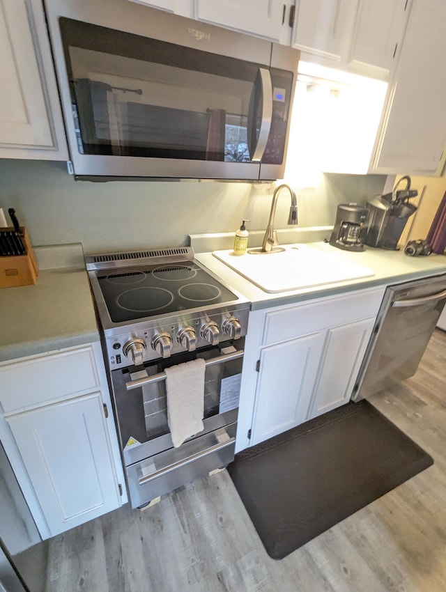 kitchen featuring white cabinetry, sink, light hardwood / wood-style floors, and appliances with stainless steel finishes