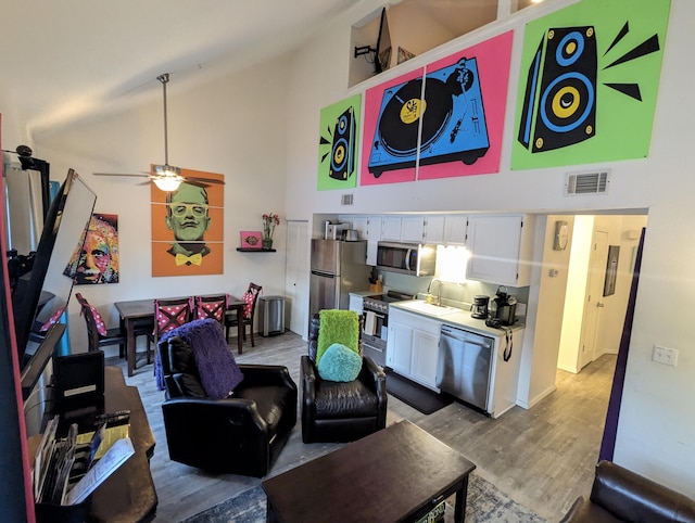 living room featuring ceiling fan, sink, high vaulted ceiling, and light hardwood / wood-style flooring