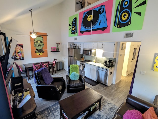 living room with hardwood / wood-style floors, high vaulted ceiling, ceiling fan, and sink