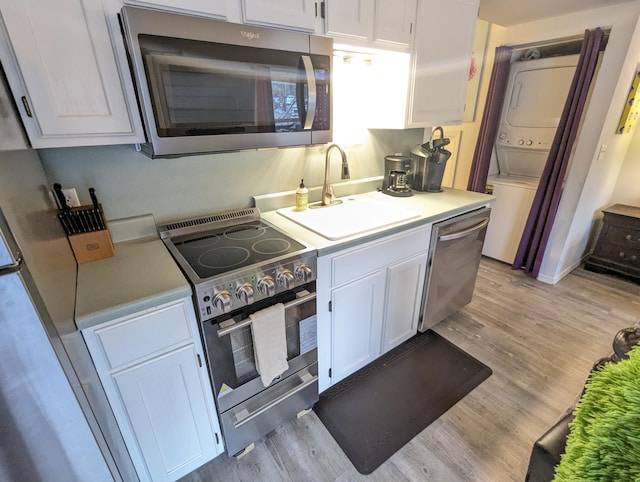 kitchen with white cabinets, stacked washing maching and dryer, sink, and appliances with stainless steel finishes