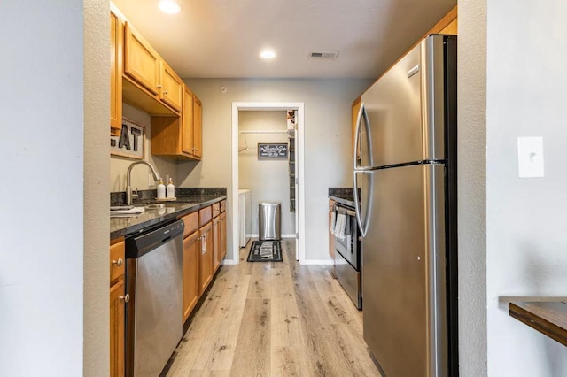 kitchen featuring dark stone counters, sink, stainless steel appliances, and light hardwood / wood-style flooring