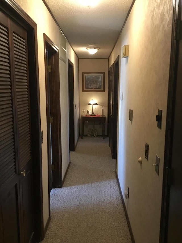 corridor featuring light colored carpet, baseboards, and a textured ceiling