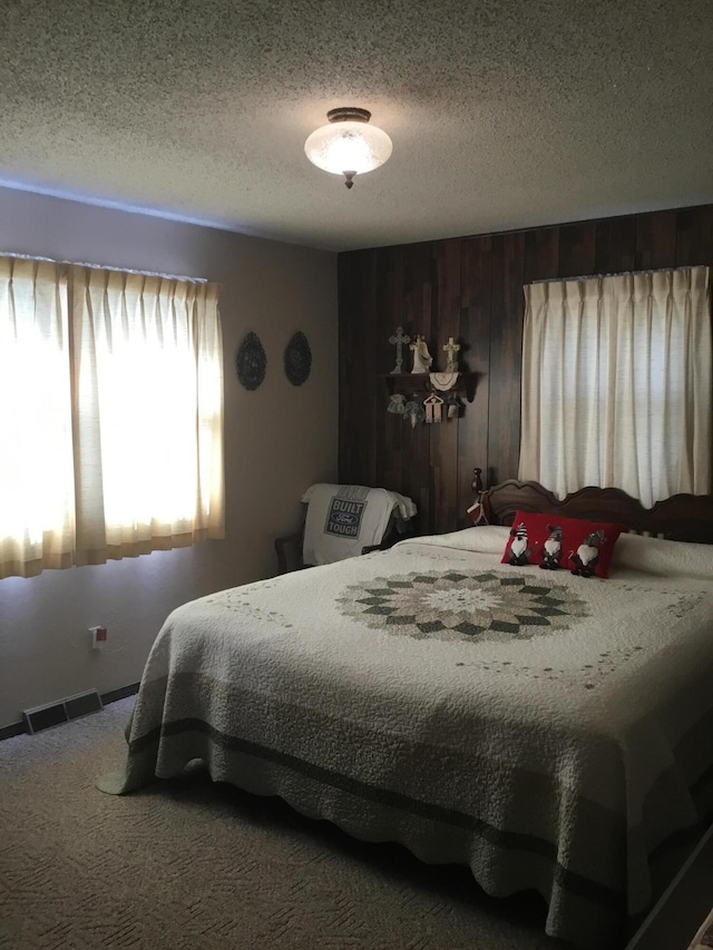 bedroom with carpet, a textured ceiling, and wooden walls