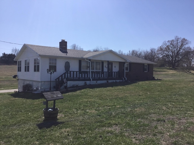 single story home featuring a porch, a chimney, a front yard, and a shingled roof