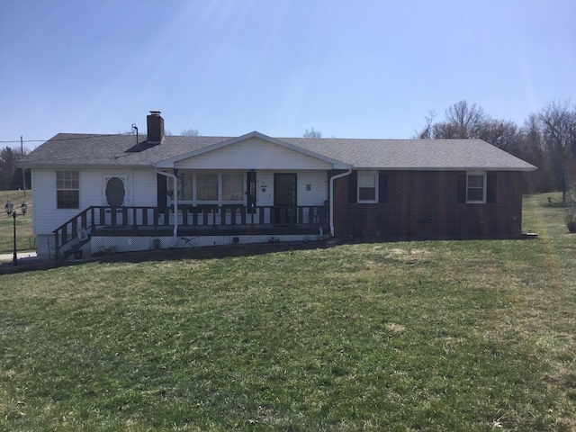 rear view of house featuring a yard, covered porch, brick siding, and a chimney