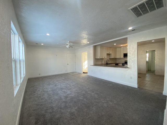 unfurnished living room featuring ceiling fan, sink, carpet, and a healthy amount of sunlight