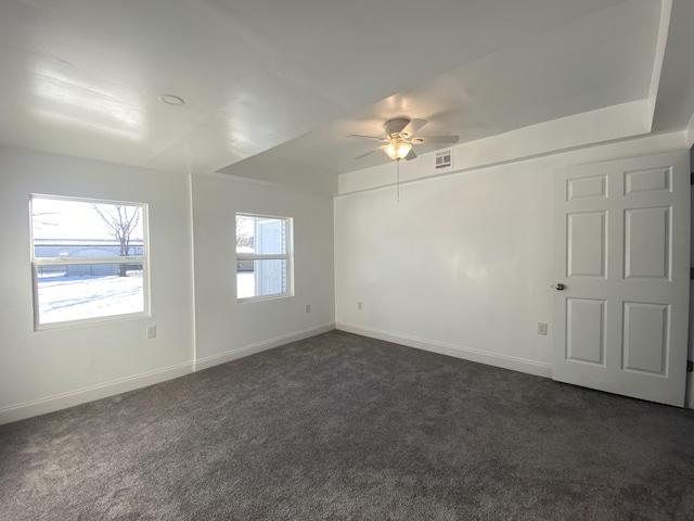 carpeted spare room featuring ceiling fan, a raised ceiling, and a wealth of natural light