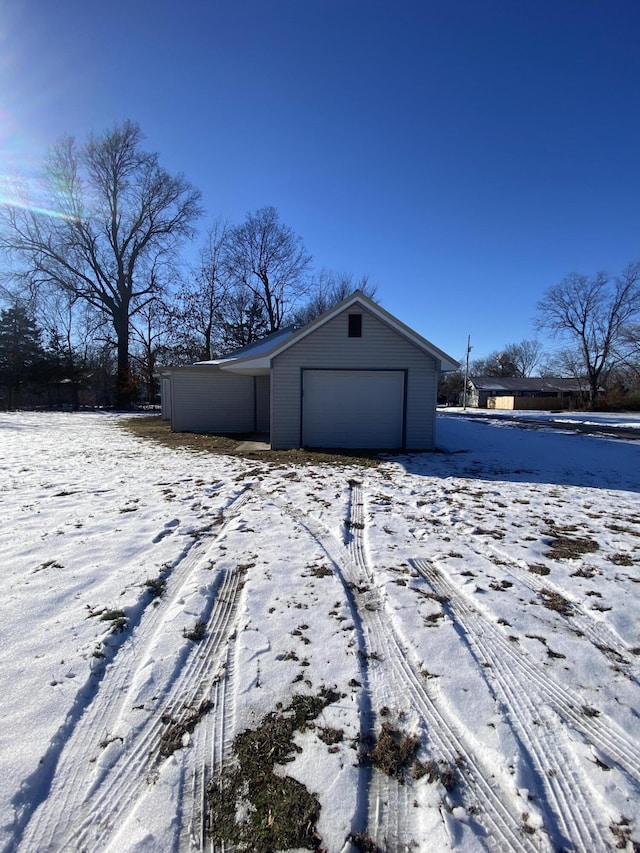 view of snow covered exterior featuring a garage and an outbuilding