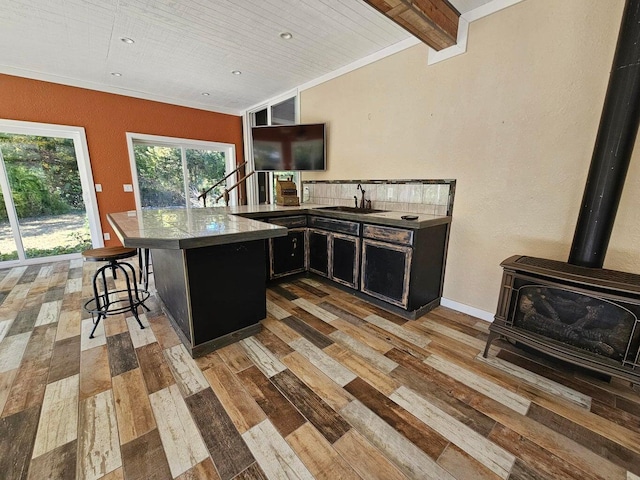 kitchen featuring light hardwood / wood-style floors, a wood stove, a breakfast bar area, beamed ceiling, and sink