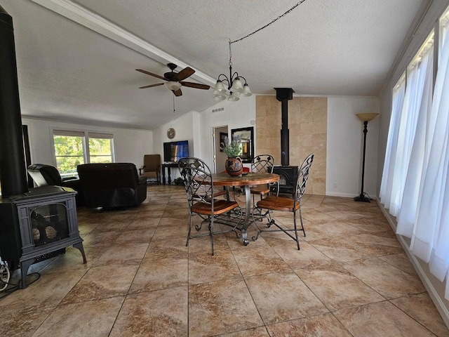 dining area with a textured ceiling, ceiling fan with notable chandelier, vaulted ceiling with beams, and a wood stove