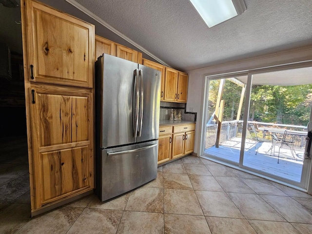 kitchen with a textured ceiling, vaulted ceiling, light tile patterned floors, decorative backsplash, and stainless steel refrigerator